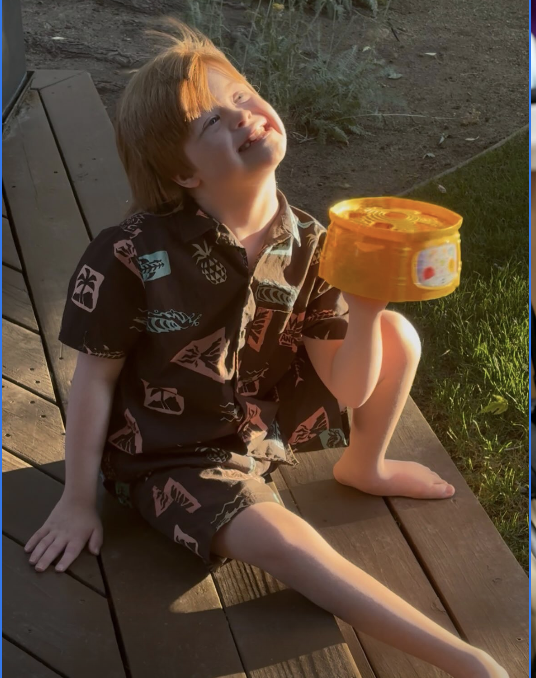 Micah smiling outdoors while holding a toy